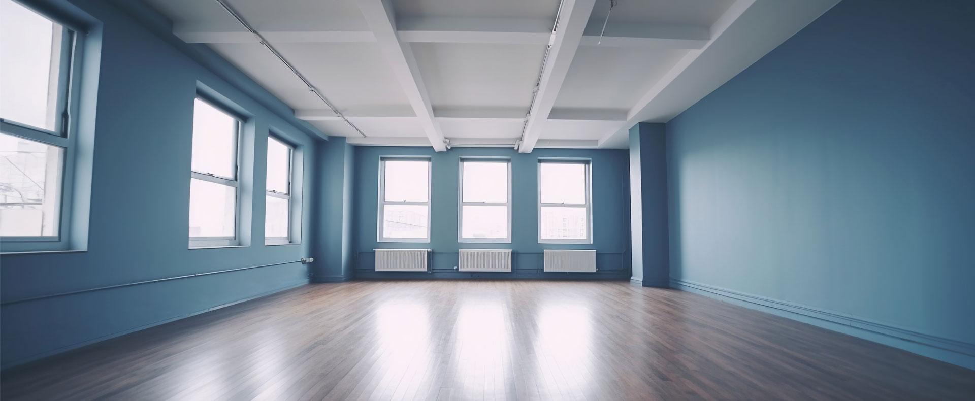 Habitación vacía con paredes recién pintadas y suelo de madera con acabado brillante.